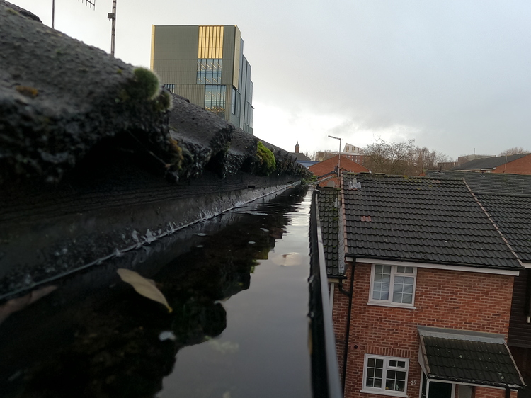 Standing water pooling in domestic gutter due to blocked outlet from sludge and moss showing overflow risk at Nottingham residential property