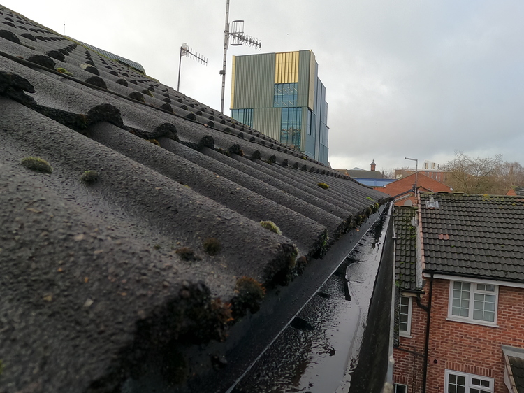 Residential roof showing heavy moss growth on tiles with blocked gutter filled with sludge requiring professional removal in Nottingham domestic property