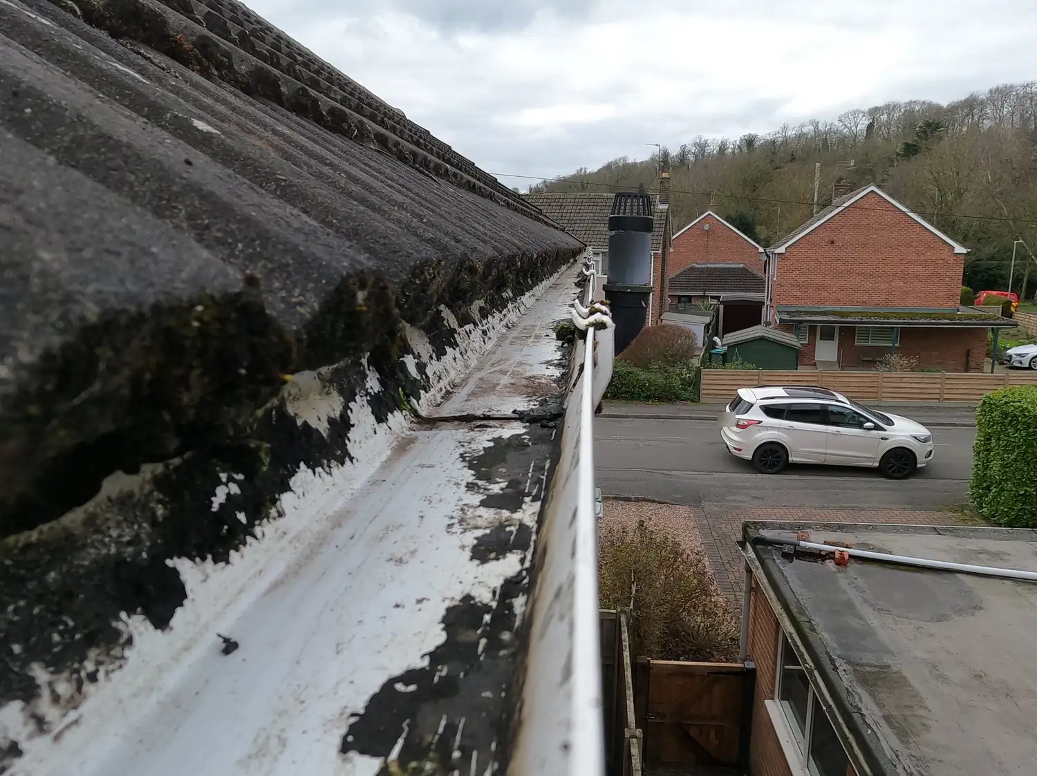 After: gutter on The Spinney, Burton Joyce, cleared to bare white plastic along its full length, with the neighbouring houses and the wooded hillside behind